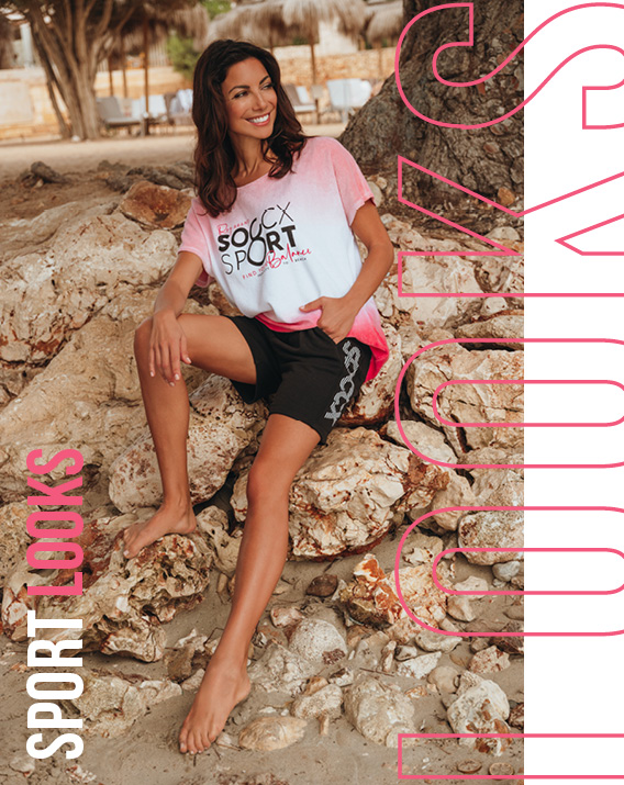 Model sitzt auf Steinen und trägt ein rosa weißes Shirt und eine schwarze Shorts