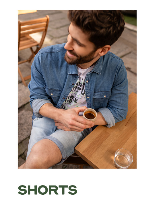 Model trägt Jeansoutfit und sitzt im Cafe.
