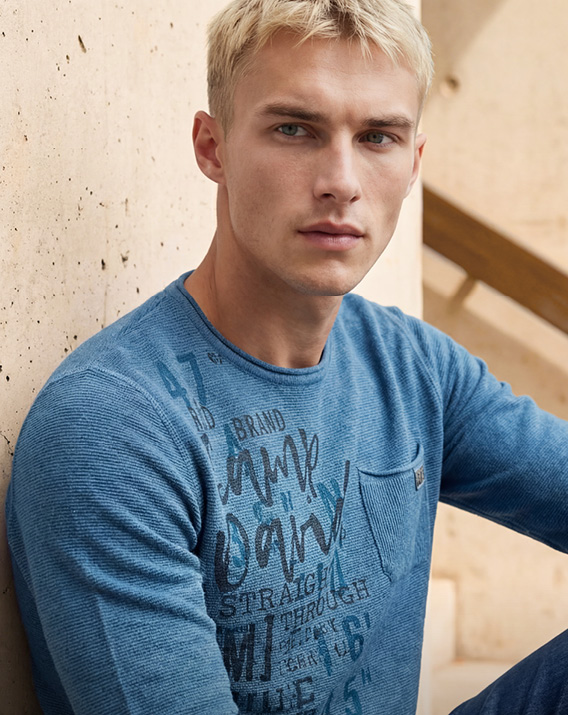 Model steht in einer Berglandschaft und trägt eine weiße Jacke