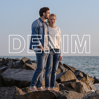 Ein Paar, was Jeans trägt, steht am Strand und sie beobachten den Horizont
