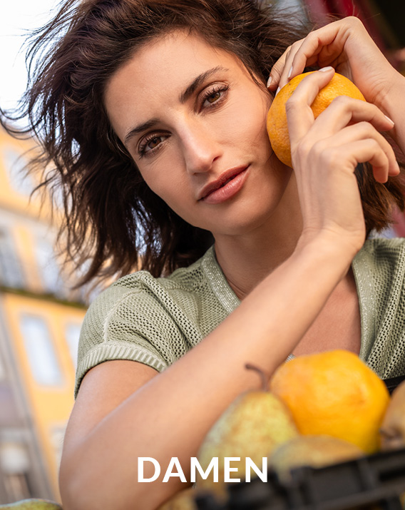 Dunkelhäutiges Model mit blauweiß gestreiften Sweatshirt lehnt mit verträumten Blick über einer Schiffsreling.