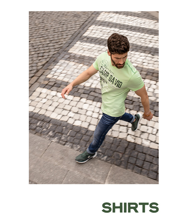 Model trägt ein grünes T-Shirt und Jeans und läuft über die Straße.